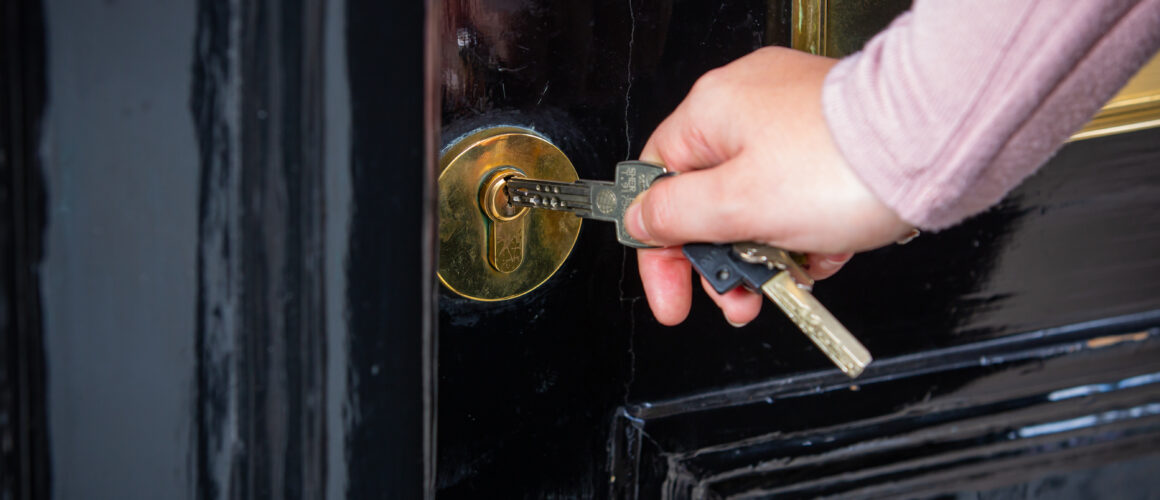 Person inserting a key into the lock of a black door.