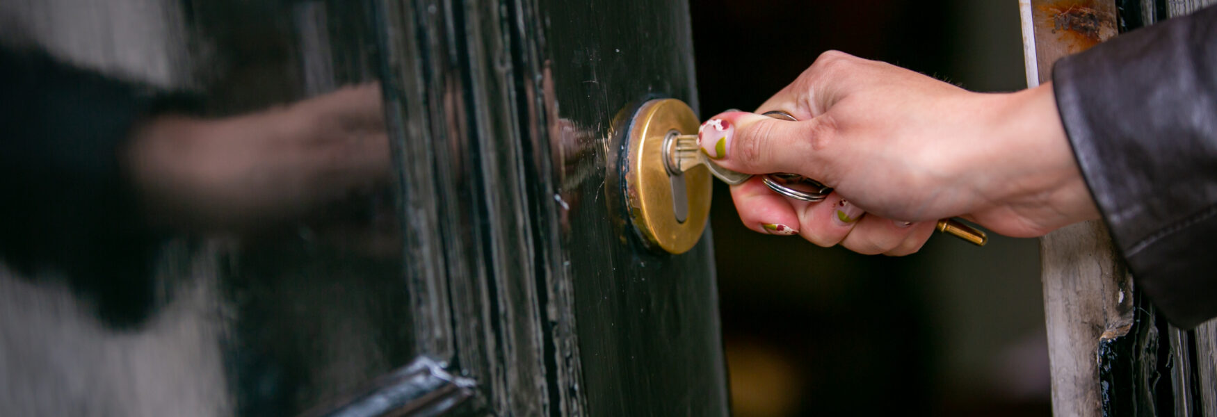 Person with colourful painted nails opening a door with a key.