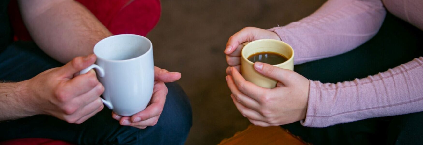 two people sitting down holding white coffee mugs